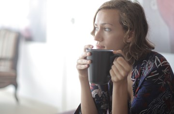 White woman sitting in corner of room holding a large mug of tea